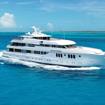 White motor yacht cruising in clear blue waters with waves trailing behind.