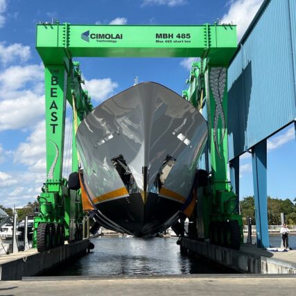 Large yacht lifted by a green boat hoist at a marina during maintenance.
