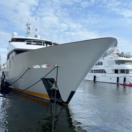 Close-up front view of a docked white yacht with other boats in the background.