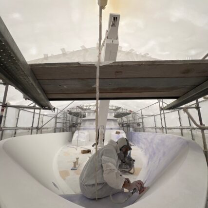 Technician in protective gear working inside a yacht hull under scaffolding.