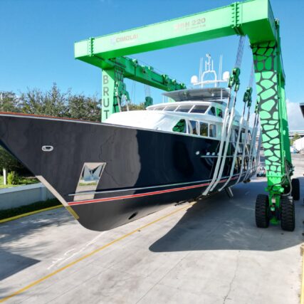 Black yacht being transported using a green boat hoist on a sunny day at the marina.